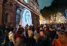 Gran afluencia de personas en el Centro Histórico de Puebla durante el festival de luz GLOW México, con proyecciones artísticas iluminando fachadas de edificios históricos de noche.