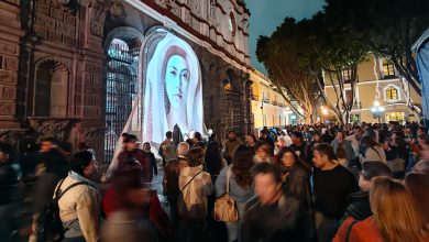 Gran afluencia de personas en el Centro Histórico de Puebla durante el festival de luz GLOW México, con proyecciones artísticas iluminando fachadas de edificios históricos de noche.