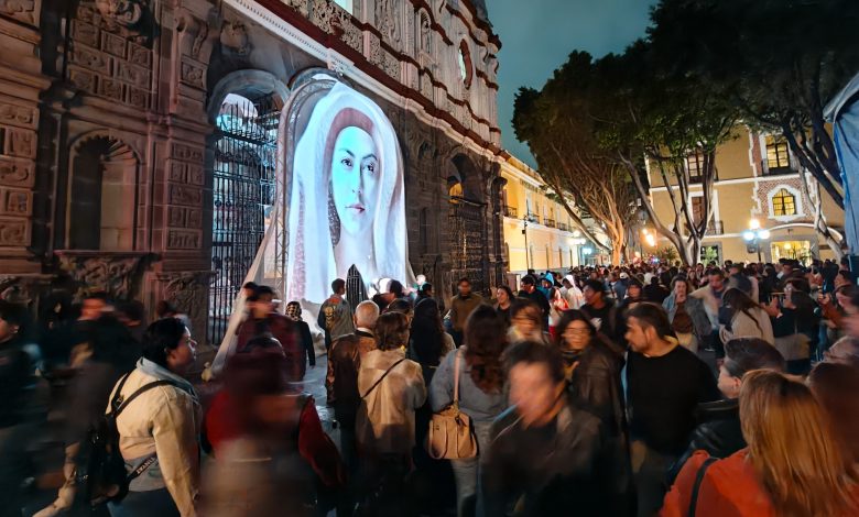 Gran afluencia de personas en el Centro Histórico de Puebla durante el festival de luz GLOW México, con proyecciones artísticas iluminando fachadas de edificios históricos de noche.