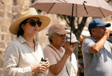 Personas caminando en una plaza soleada en Puebla, México, con sombreros, una sombrilla y botellas de agua, siguiendo las recomendaciones sanitarias contra el calor