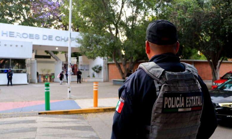 Oficial de la Policía Estatal de Puebla de espaldas, portando chaleco táctico, vigilando la entrada del Centro Escolar Niños Héroes de Chapultepec ante operativos por retos virales.