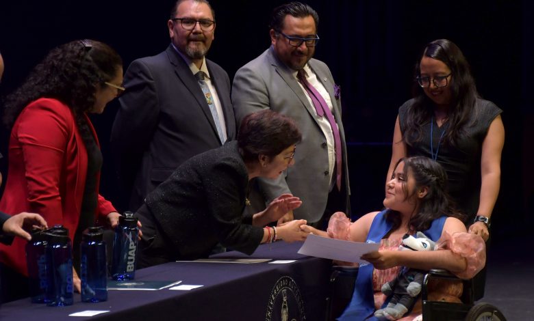 Rectora de la BUAP entrega diploma a alumna en silla de ruedas durante ceremonia de graduación de la preparatoria Emiliano Zapata.