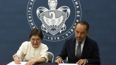Rectora de la BUAP y director de Atención Estudiantil firman documentos en una mesa, con el escudo de la universidad de fondo.
