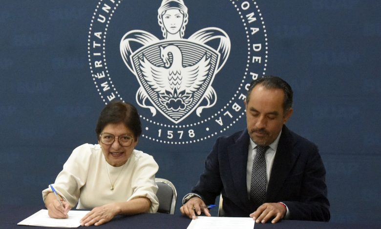 Rectora de la BUAP y director de Atención Estudiantil firman documentos en una mesa, con el escudo de la universidad de fondo.
