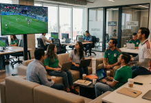 Trabajadores con camisetas de la selección mexicana siguen un partido del Mundial en una pantalla de oficina mientras trabajan con laptops.