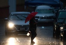 Peatón cruza la calle bajo lluvia intensa con paraguas rojo en Puebla