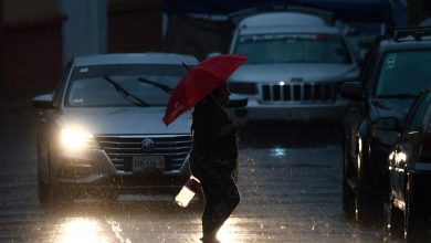 Peatón cruza la calle bajo lluvia intensa con paraguas rojo en Puebla
