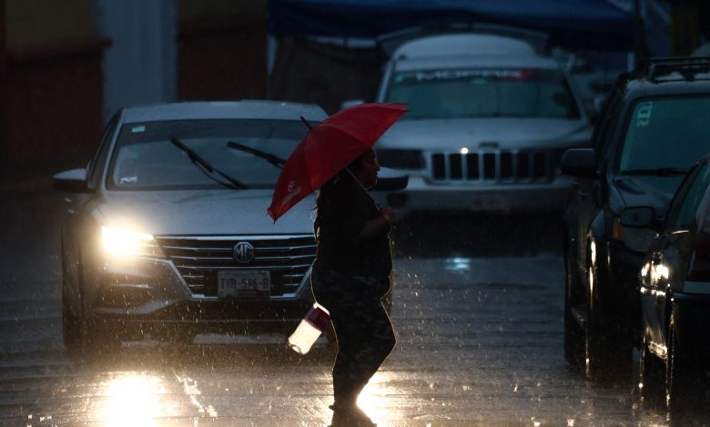 Peatón cruza la calle bajo lluvia intensa con paraguas rojo en Puebla