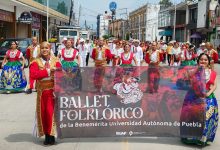 Integrantes del Ballet Folklórico de la BUAP con vestuario tradicional sostienen una lona con el nombre del grupo durante un desfile en San Martín Texmelucan.