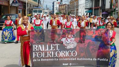 Integrantes del Ballet Folklórico de la BUAP con vestuario tradicional sostienen una lona con el nombre del grupo durante un desfile en San Martín Texmelucan.