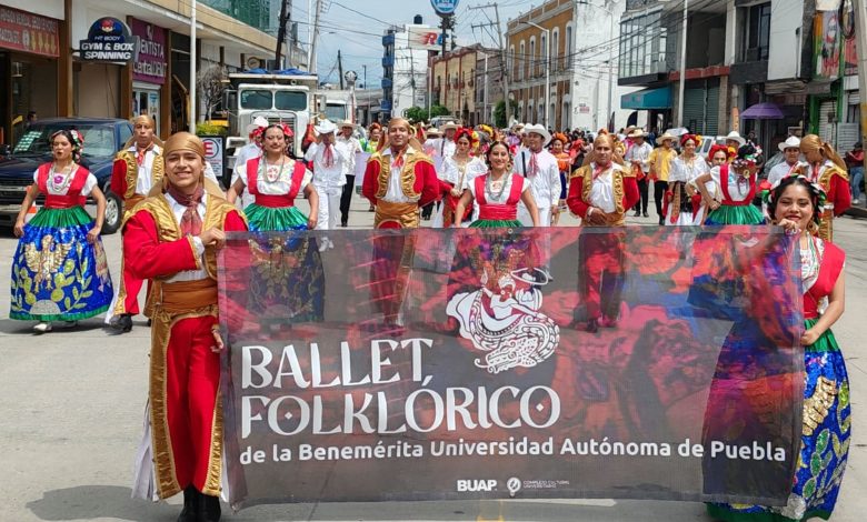 Integrantes del Ballet Folklórico de la BUAP con vestuario tradicional sostienen una lona con el nombre del grupo durante un desfile en San Martín Texmelucan.
