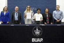 Autoridades de la BUAP y de la Secretaría de Desarrollo Turístico de Puebla muestran el convenio de colaboración firmado, de pie tras una mesa con el escudo de la BUAP.