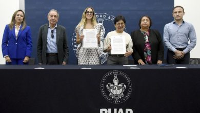 Autoridades de la BUAP y de la Secretaría de Desarrollo Turístico de Puebla muestran el convenio de colaboración firmado, de pie tras una mesa con el escudo de la BUAP.