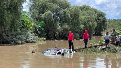 Patrulla de la Policía Municipal semihundida en el río Atoyac durante las maniobras de rescate en Ocoyucan; un buzo se sumerge junto a la unidad mientras elementos de rescate y militares trabajan desde la orilla.