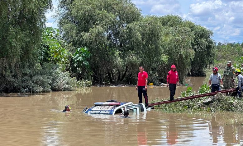 Patrulla de la Policía Municipal semihundida en el río Atoyac durante las maniobras de rescate en Ocoyucan; un buzo se sumerge junto a la unidad mientras elementos de rescate y militares trabajan desde la orilla.